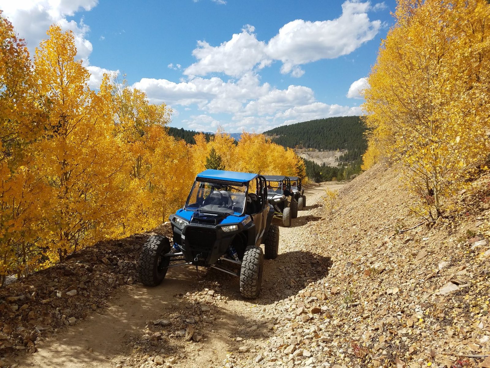 A Polaris RZR leading UTVs down a rocky mining road between gold aspens above Leadville